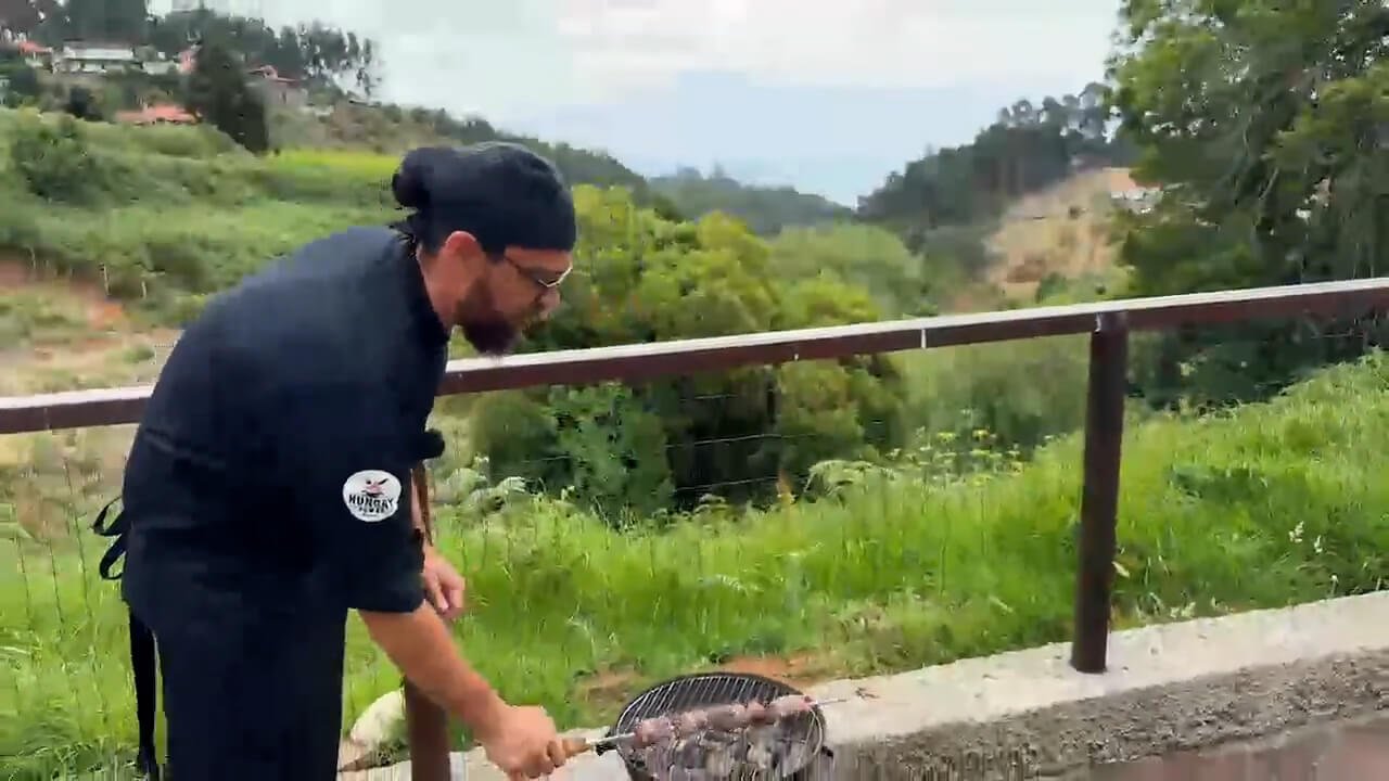Chef Sergio grilling traditional Madeira beef espetada over charcoal in the countryside of Santo da Serra